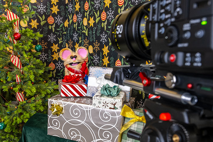 Buttons the Christmas Mouse rod puppet on set in front of the camera during filming of the I Spot Santa episode.