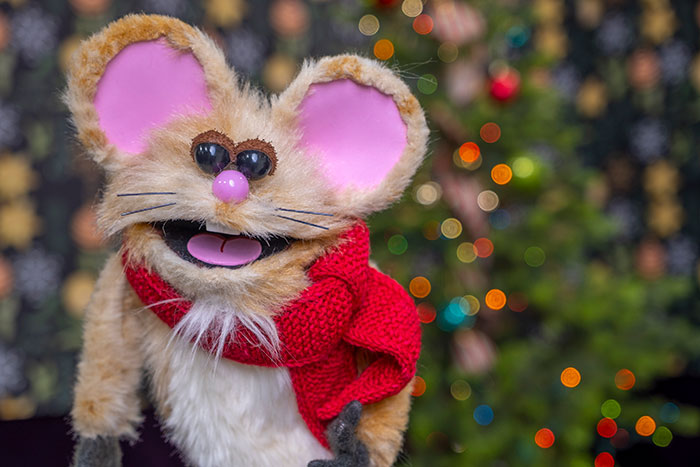 Buttons the Christmas Mouse rod puppet wearing his red scarf beside the decorated tree.